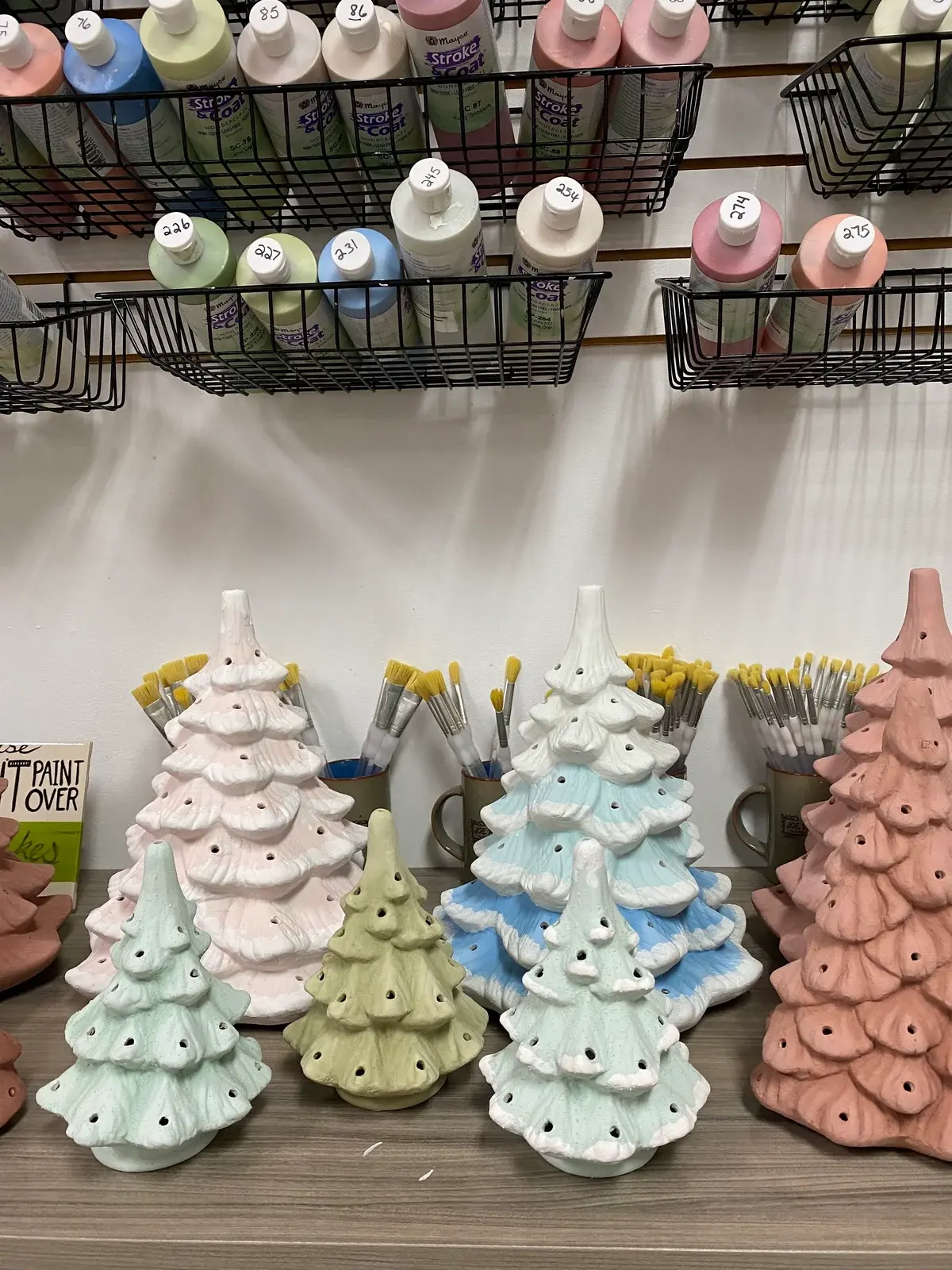Ceramic Christmas trees in pastel glazes beside paintbrushes at Joe Picasso’s studio